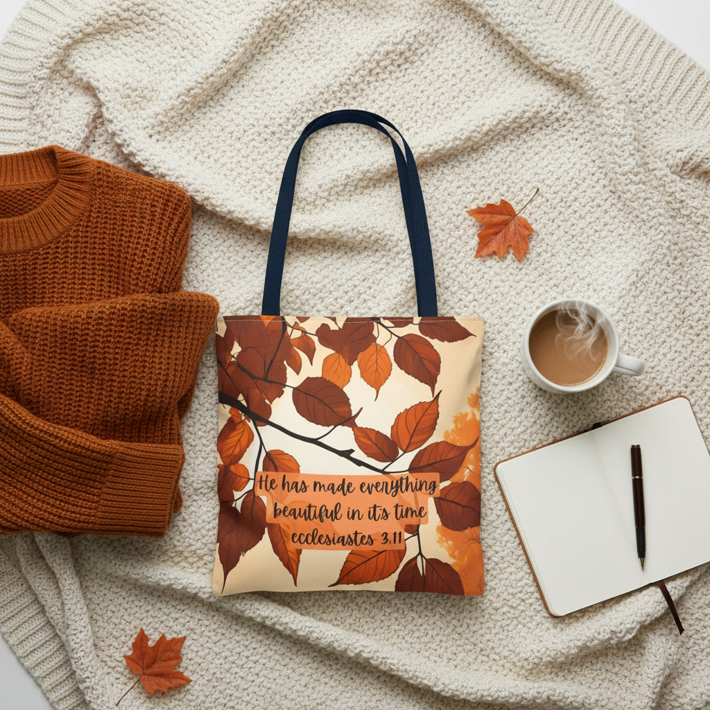 A tote bag with black handles, featuring a printed design of brown and orange autumn leaves on a cream background with the text 'He has made everything beautiful in its time ecclésiastes 3:11'.